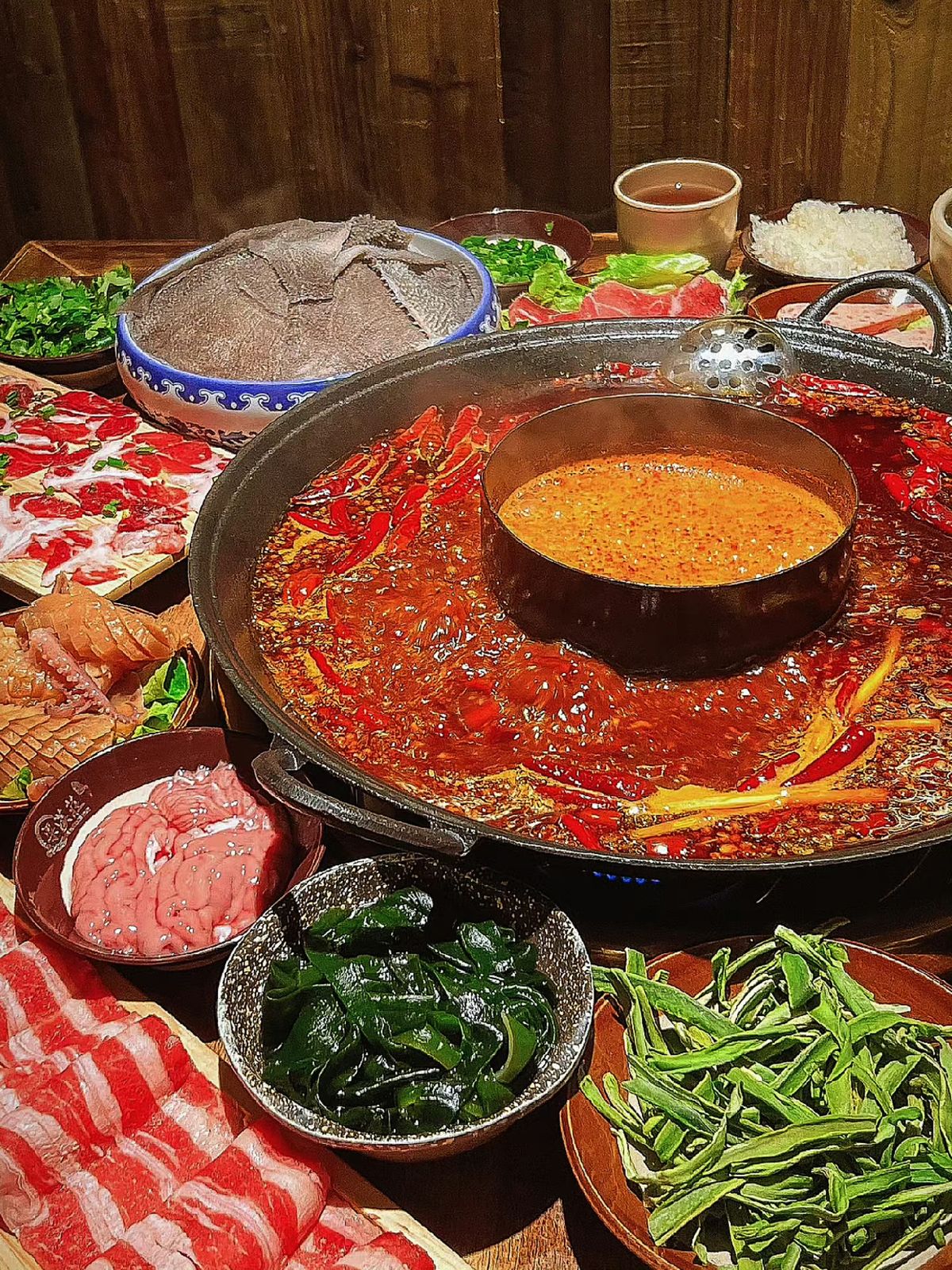 หม้อไฟหม่าล่าอู่หยวนหยาง ซีกนอกพริกแดงเต็มน้ำมันเดือด ซีกในน้ำซุปส้มสด ล้อมรอบด้วยจานหมูสไลด์ เนื้อวัว ตับ สาหร่าย ผักบุ้ง ข้าวสวย น้ำจิ้ม